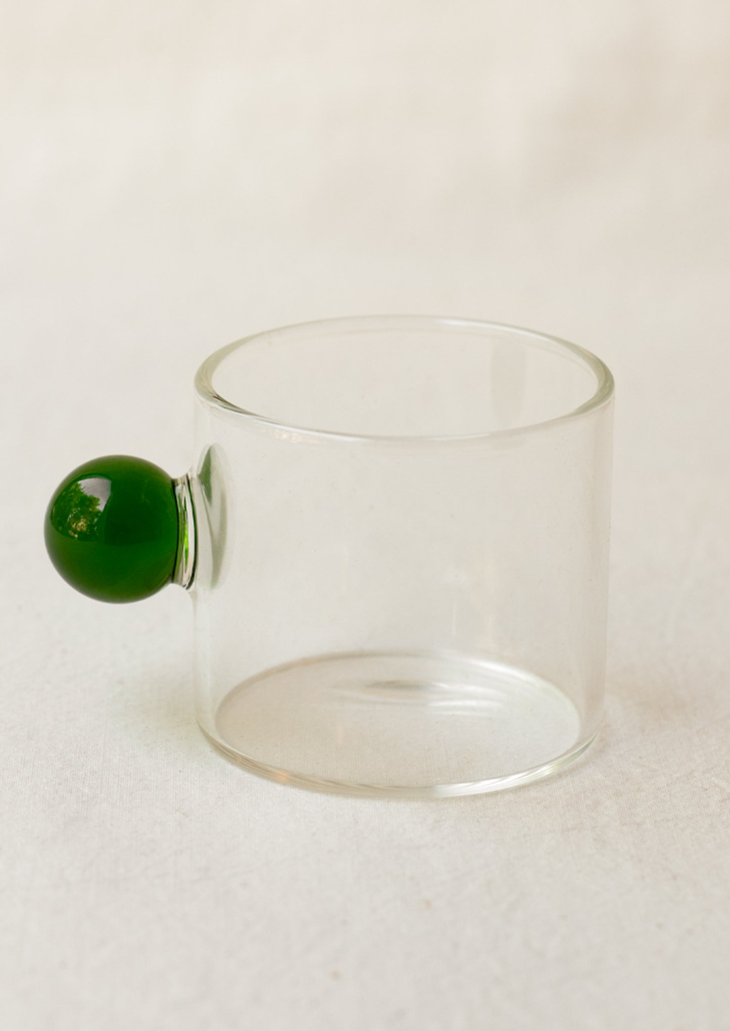 A clear glass cylindrical cup with round knob handle in green.