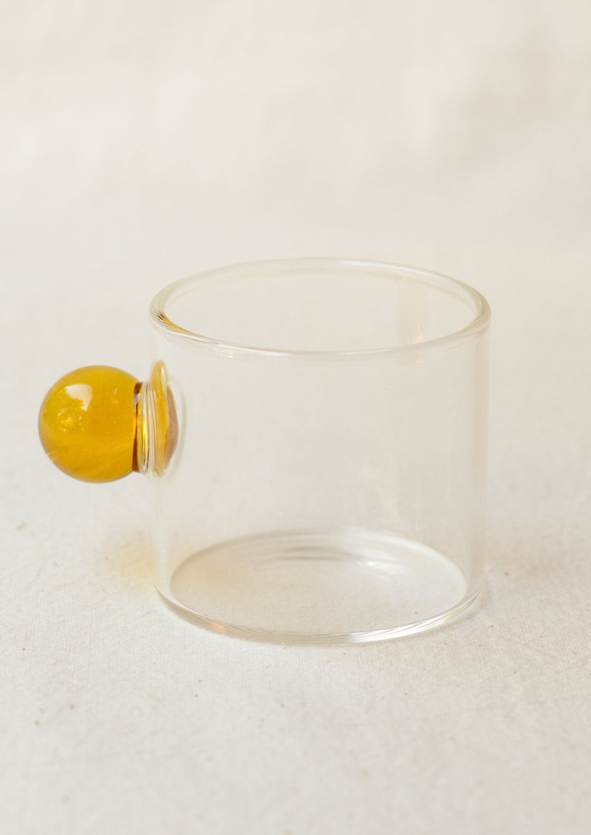 A clear glass cylindrical cup with round knob handle in yellow.