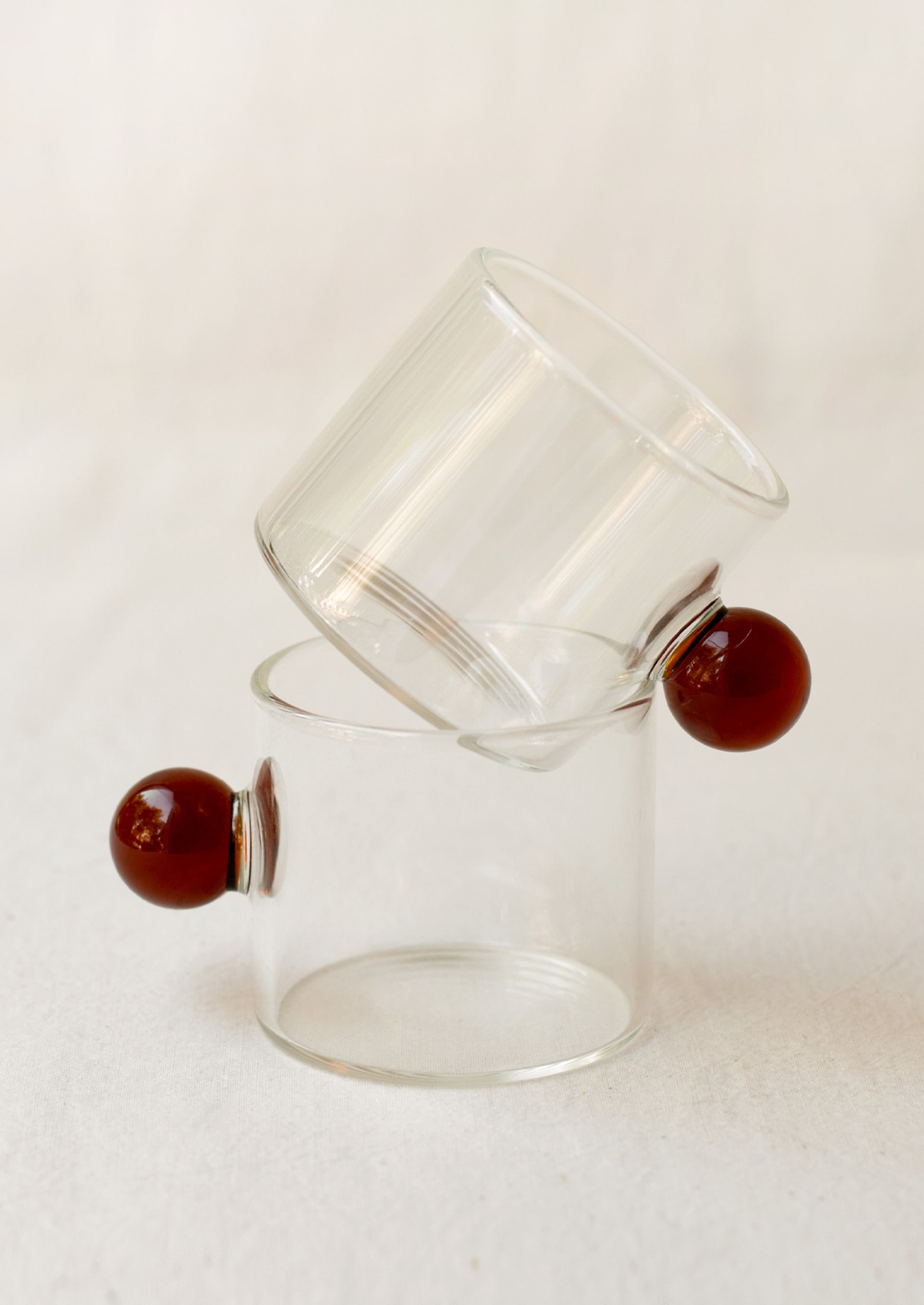 A clear glass cylindrical cup with round knob handle in brown.