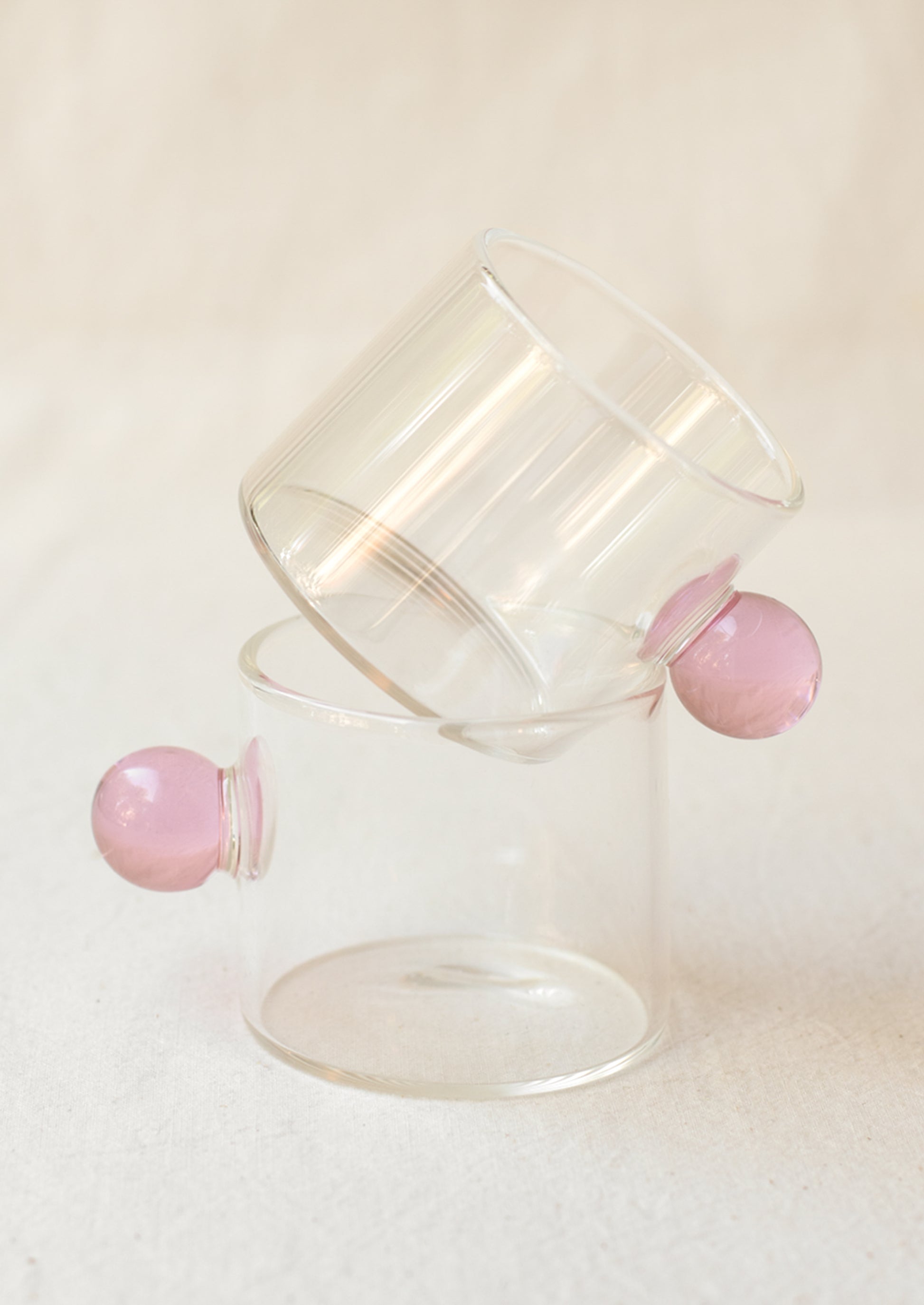 A clear glass cylindrical cup with round knob handle in pink.