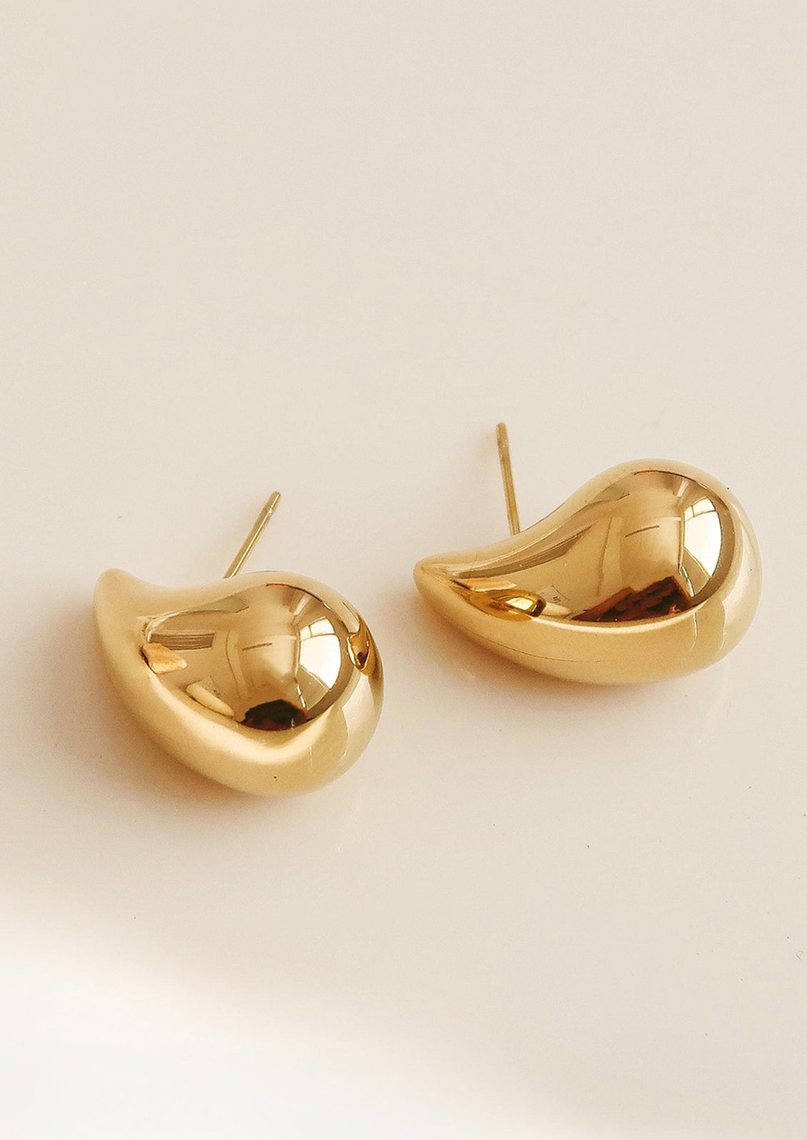 A pair of chunky, teardrop-shaped earrings in gold.
