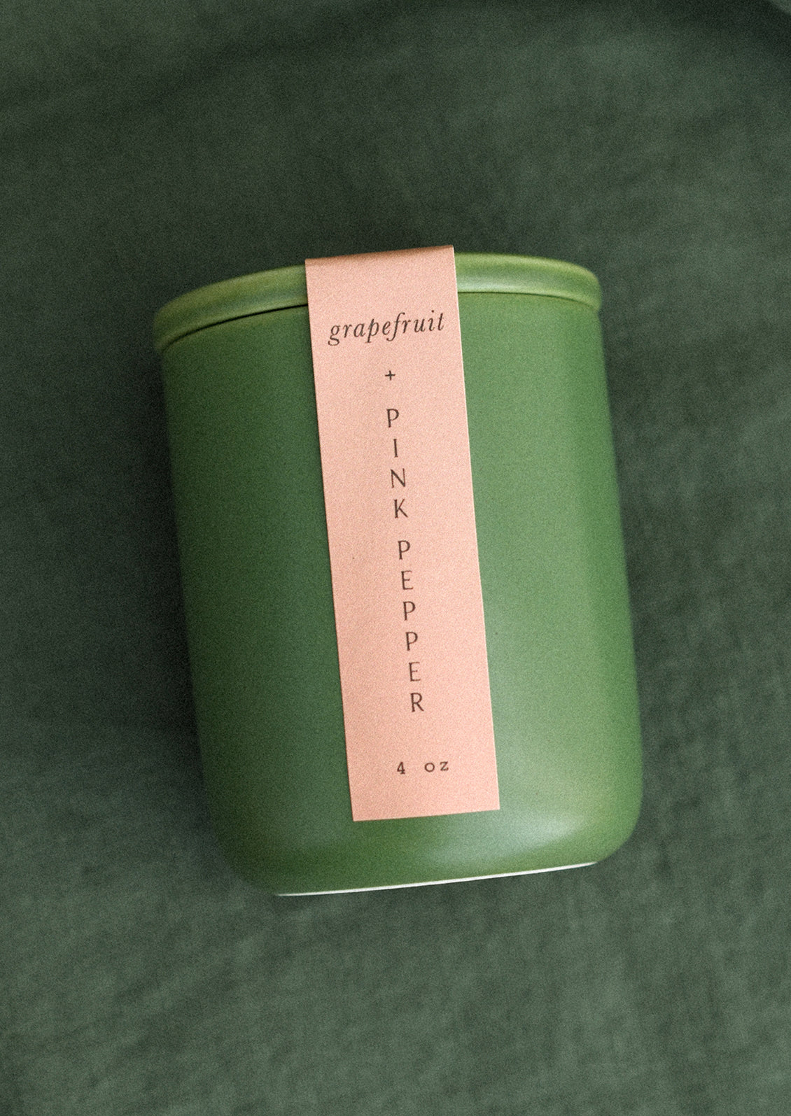 A small candle in lidded green ceramic jar in Grapefruit and Pink Pepper scent.