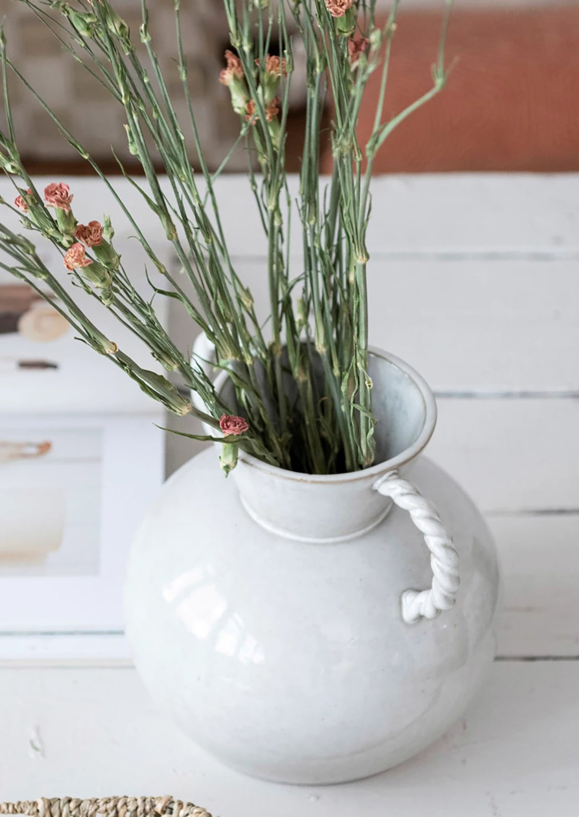 A white ceramic vase in situ with carnations.