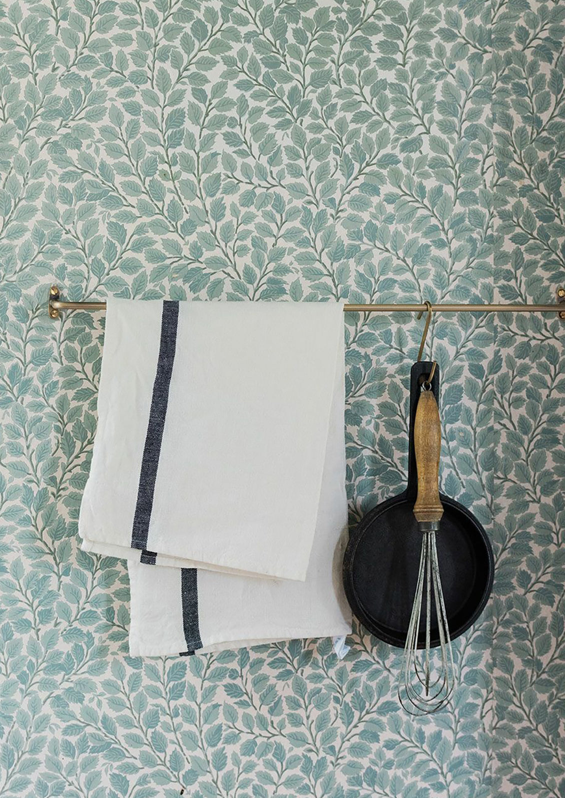 A brass bar holding a pot, whisk and tea towel.