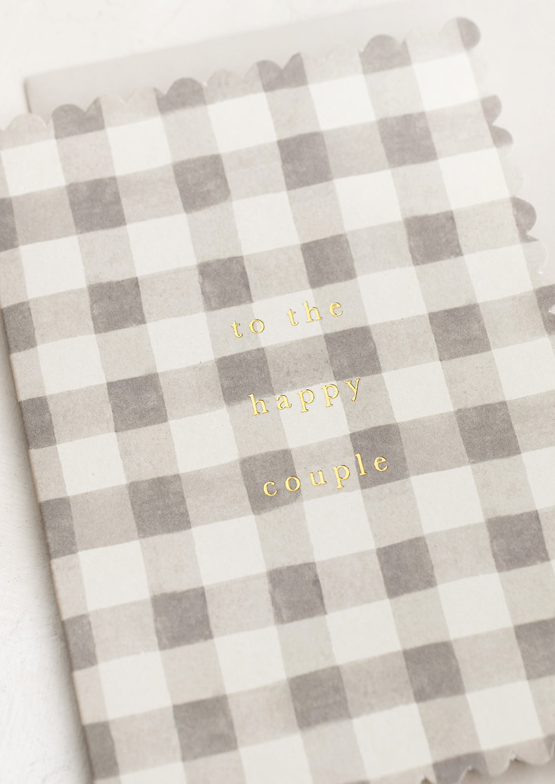 A scalloped edge card with grey gingham pattern reading "To the happy couple".