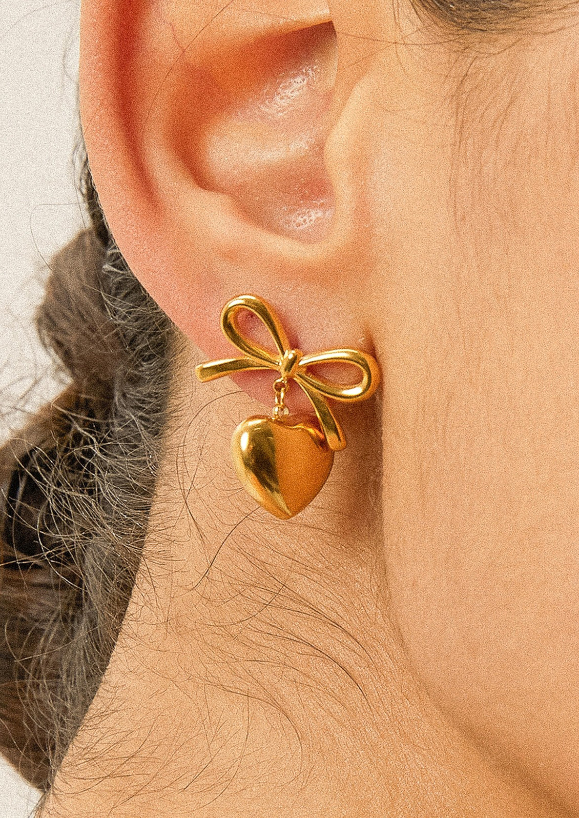 A pair of gold earrings with dangling heart charm and bow shaped post.