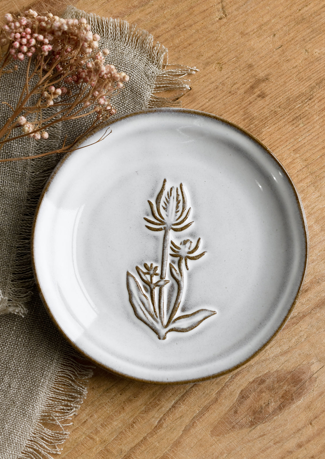 A grey glazed brown clay mini plate with raised flower design.