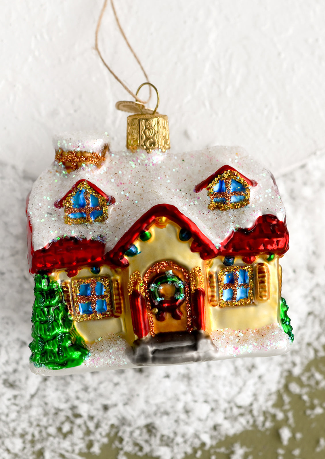 A glass holiday ornament of a house decorated for the holidays.