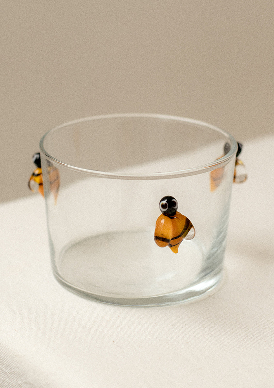 A clear glass cup in shallow shape with lampwork bee detail on outside.