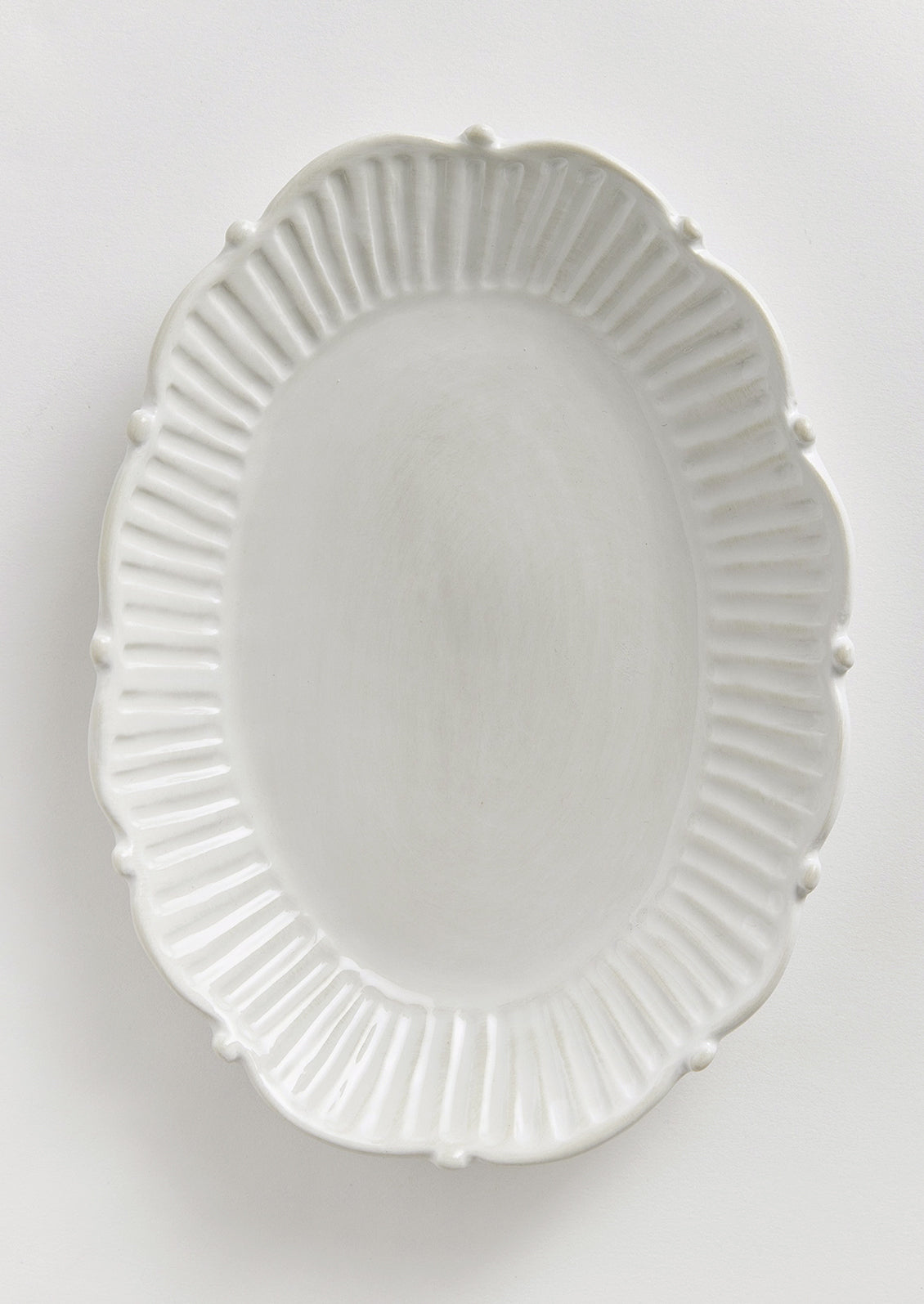 An oval shaped tray with ruffled and pleated border with ball detail around edges.