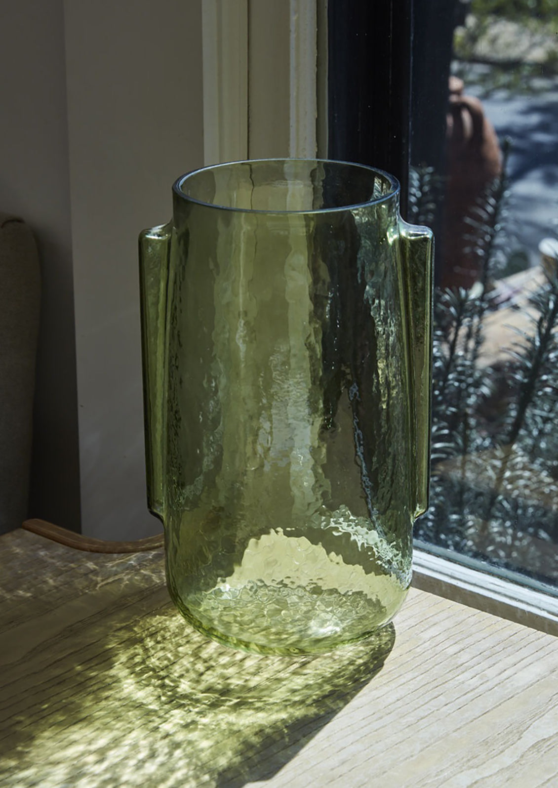 A transparent green glass vase in tall shape with side handle detail.