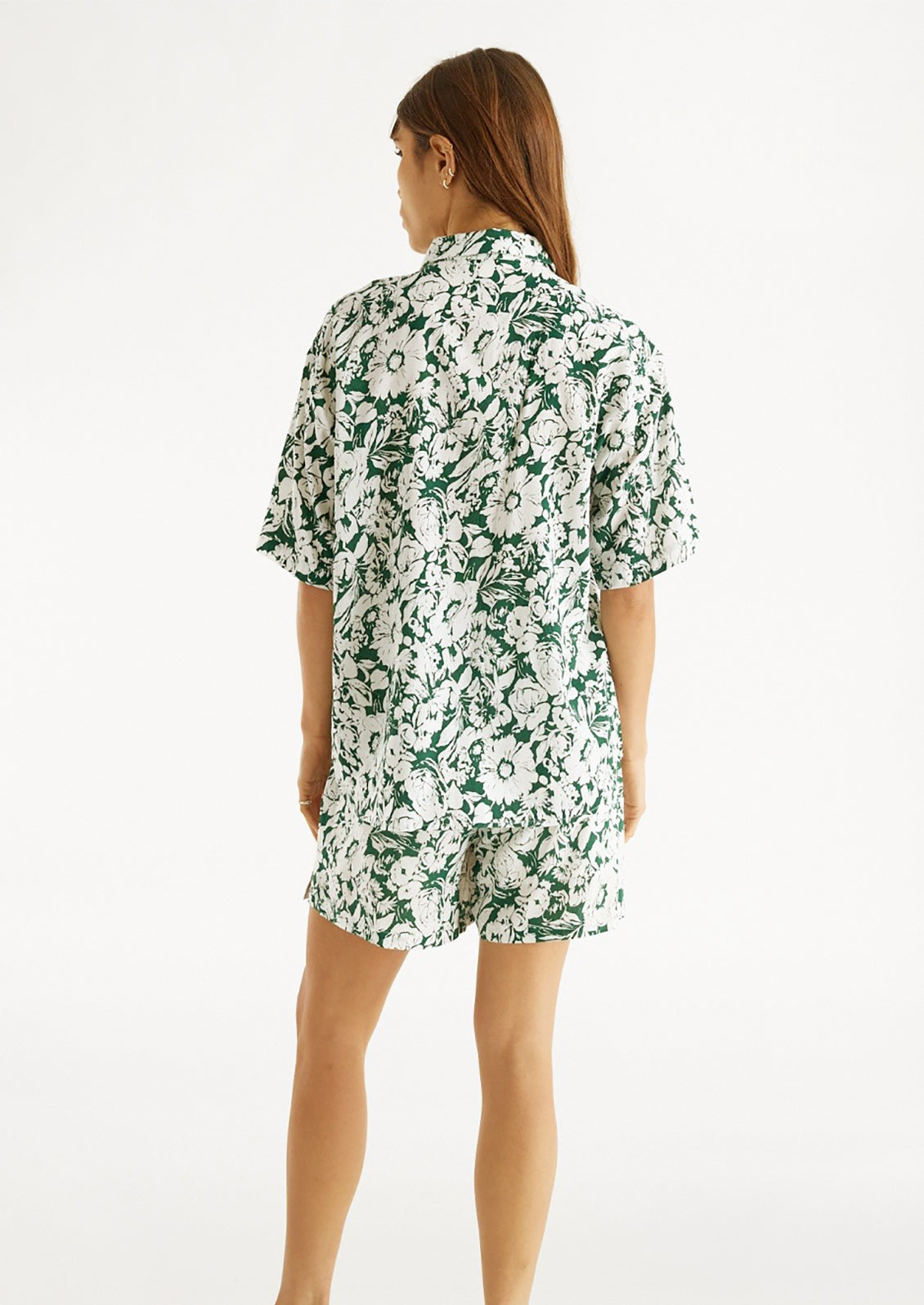 Woman wearing green and white floral printed shorts and matching shirt, seen from behind. 