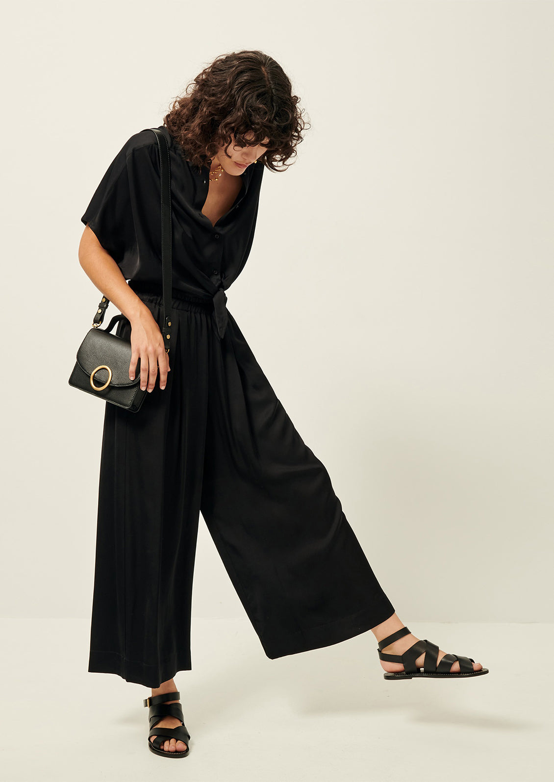 Woman wearing black flowy pants, black button-up, sandals, and purse.