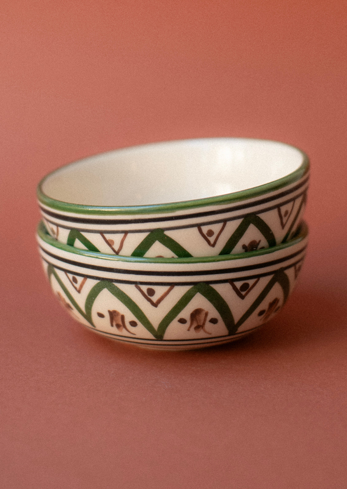 A small ceramic pinch bowl in cream with Moroccan-inspired painted geometric design in green and brown.