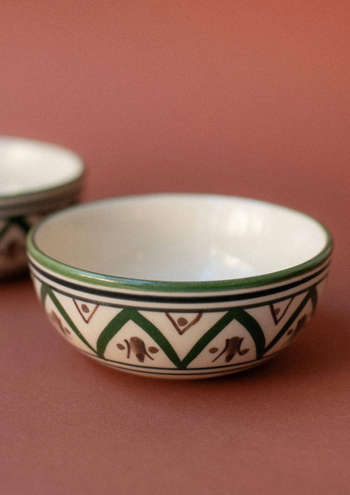 A small ceramic pinch bowl in cream with Moroccan-inspired painted geometric design in green and brown.