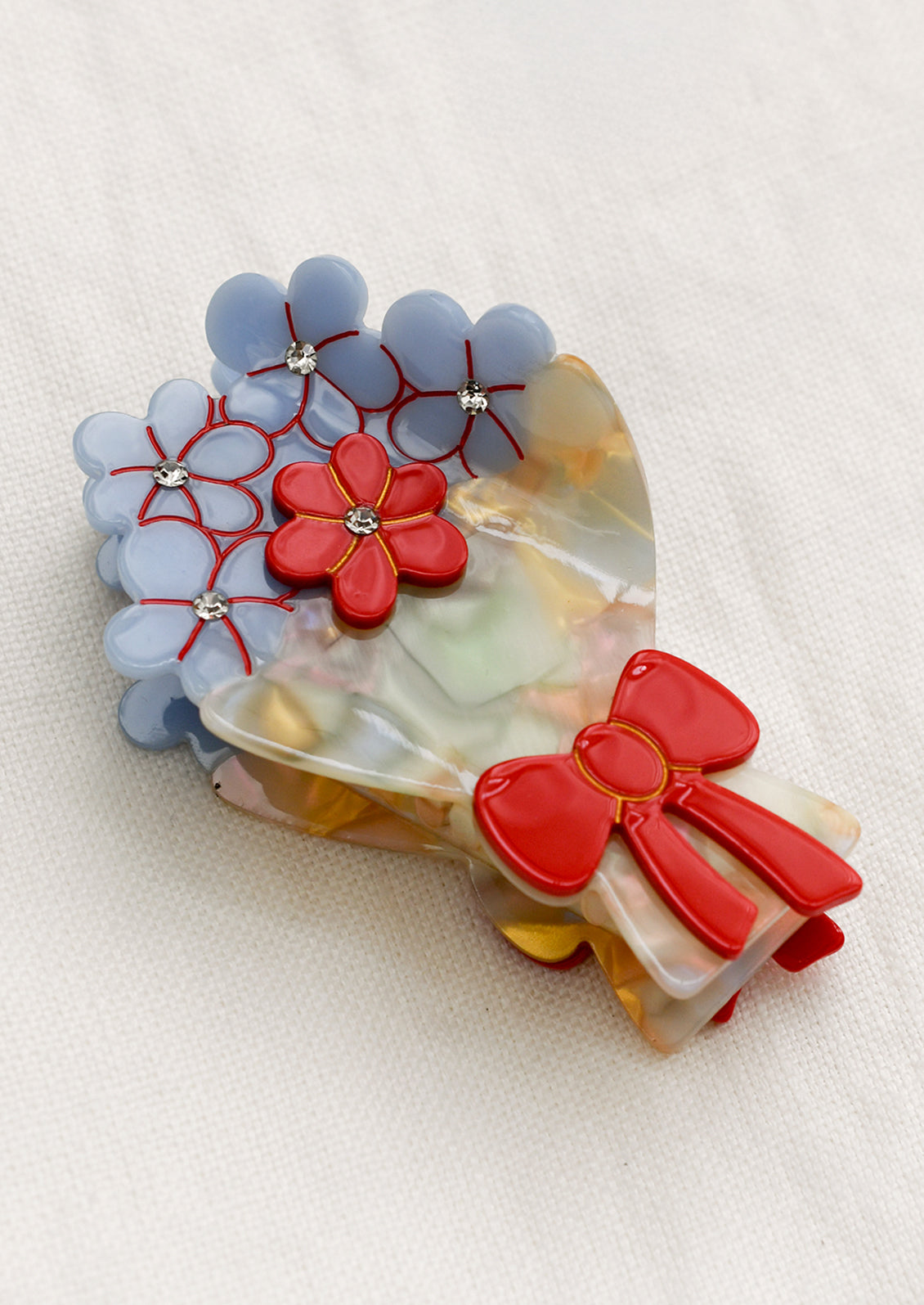 A hair claw in the shape of bouquet, with red bowl and blue and red flowers with rhinestone detailing.