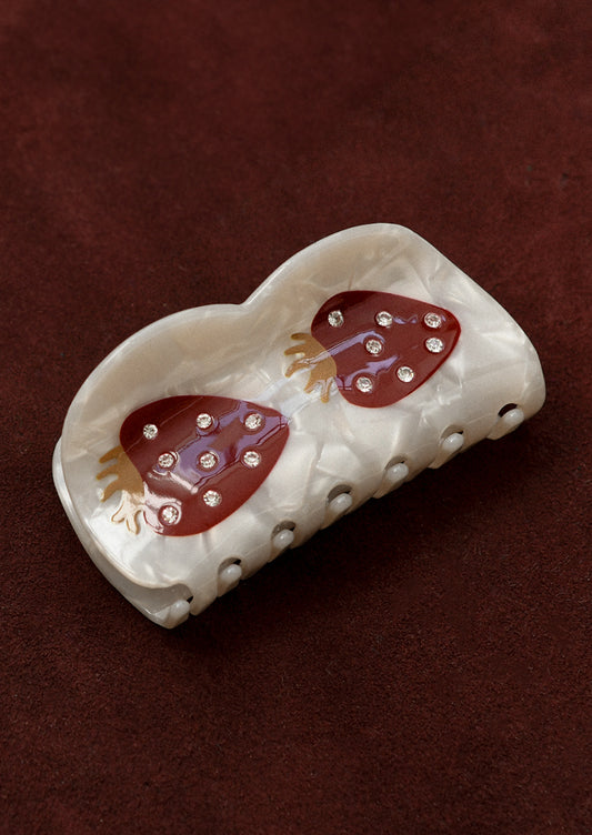 A pearlized hair claw with curvy shape and dark red strawberry with crystal detailing.