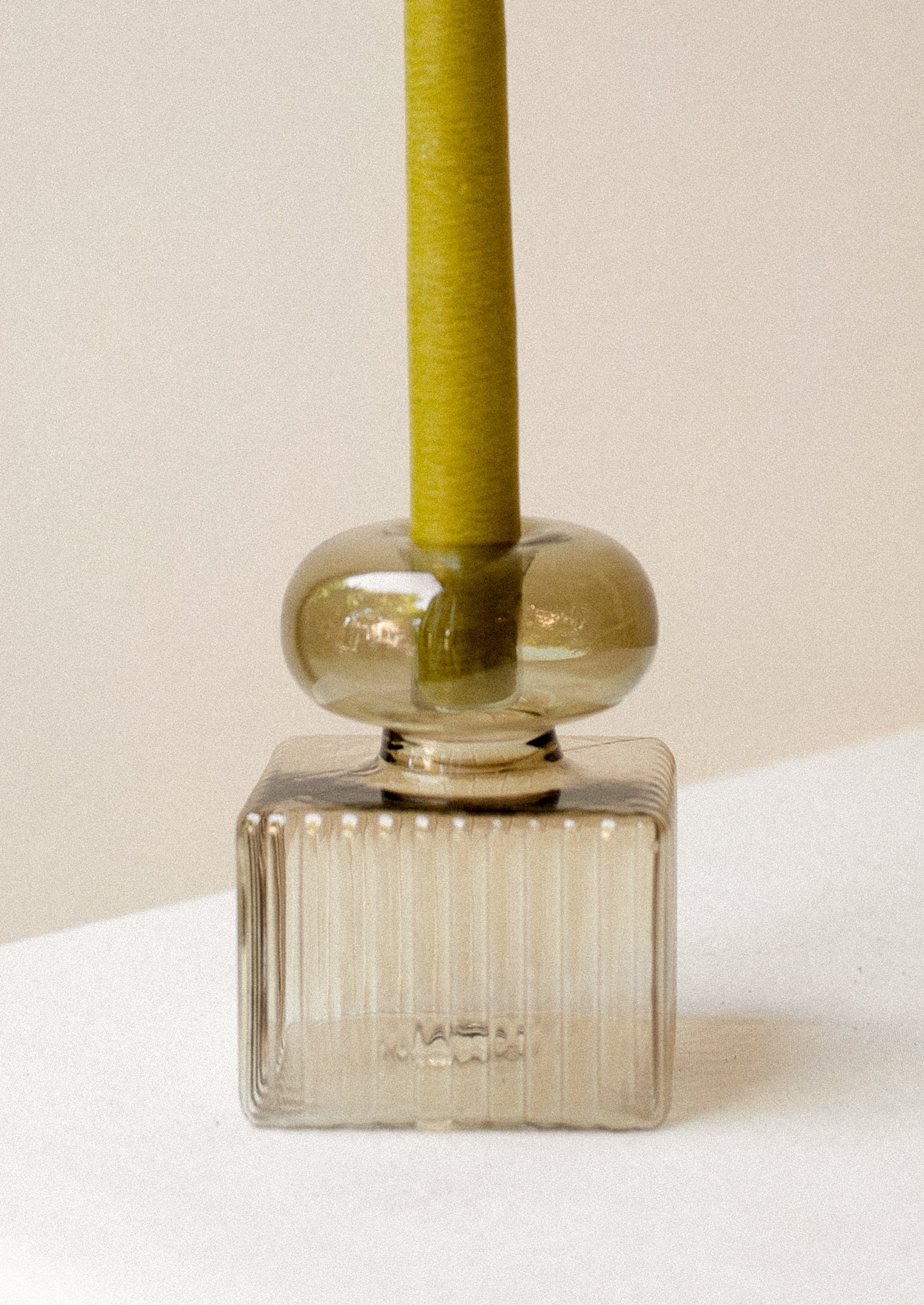 A transparent glass candleholder in olive green with round top, and ribbed square bottom.