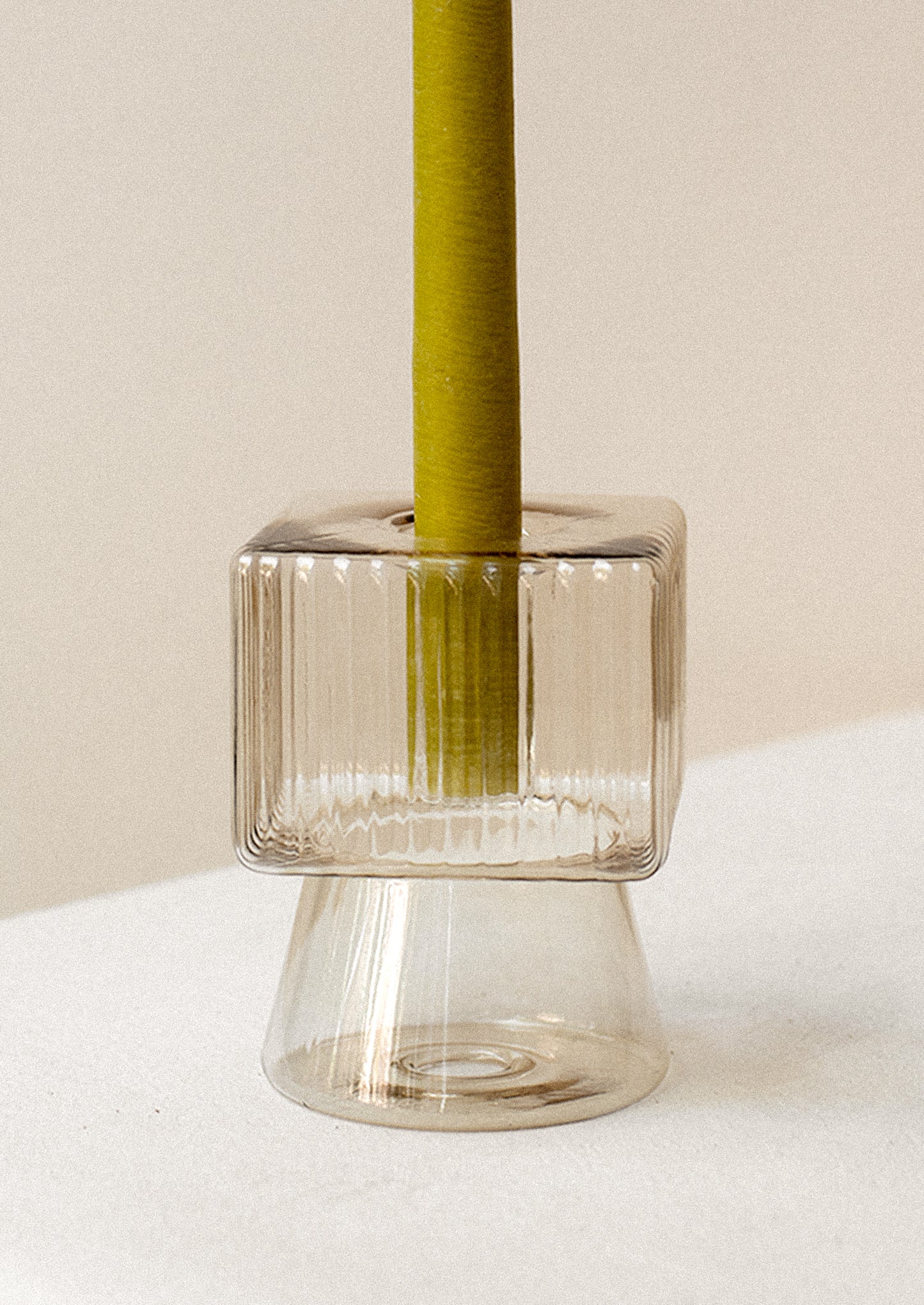 A transparent glass candleholder in tan with ribbed square top and cone shaped bottom.