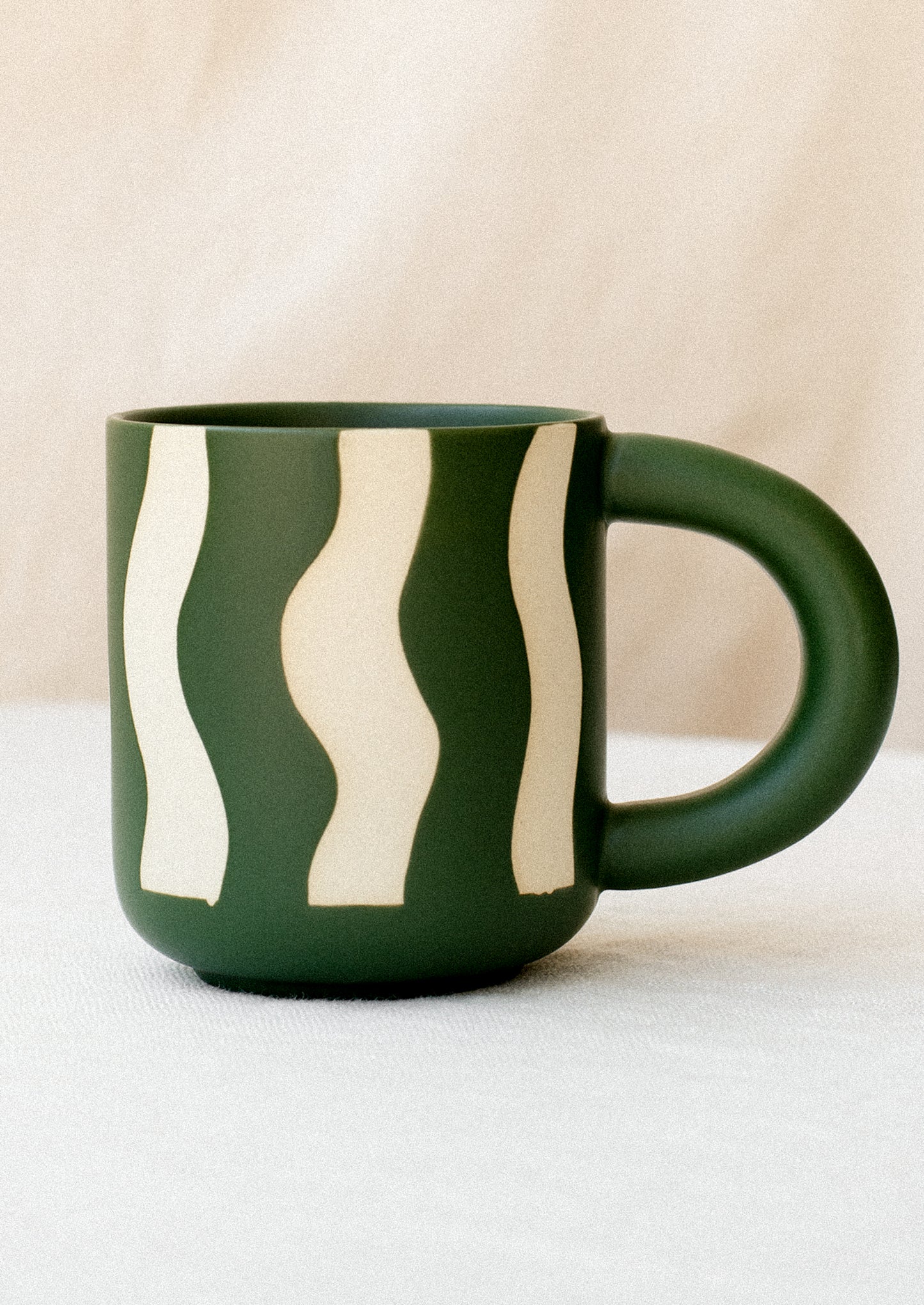 A ceramic mug in dark green with wax relief wavy stripe pattern.