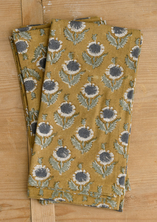 A pair of block printed napkins in ochre with muted dark grey and sage green floral pattern.