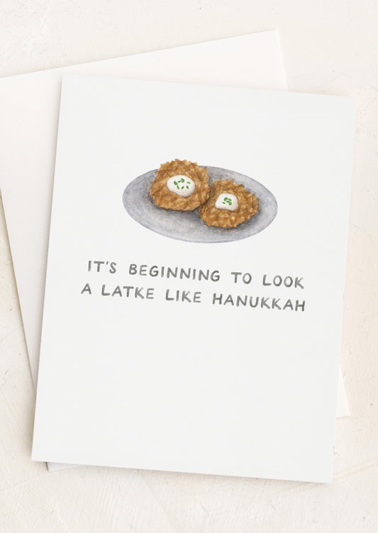 A greeting card with illustration of latkes and text reading "It's beginning to look a latke like Hanukkah".