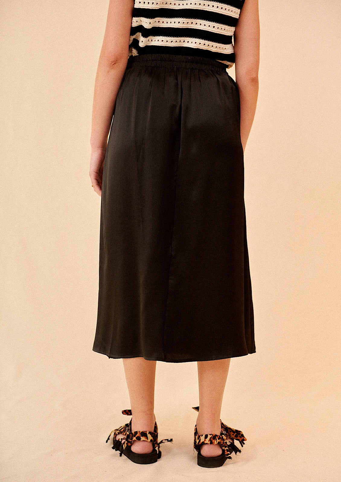 Woman wearing black midi skirt and sandals, seen from behind. 