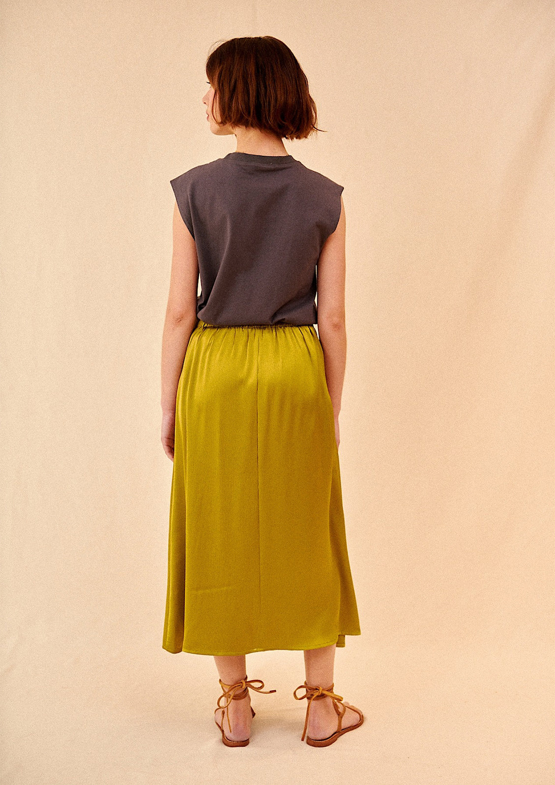 Woman wearing olive green midi skirt, t-shirt, and sandals, seen from behind. 