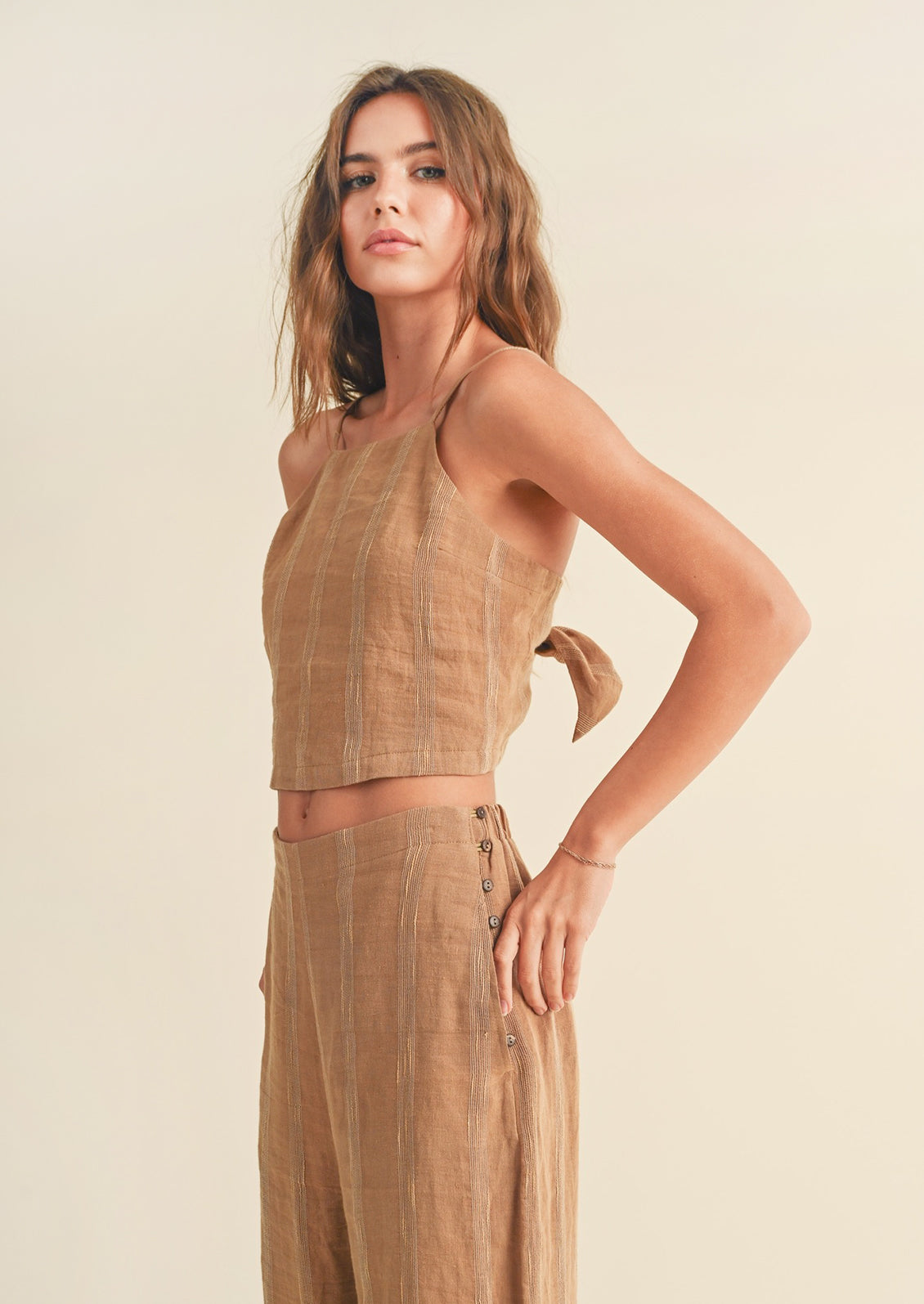 A woman wearing a sleeveless, thin strap brown linen tank with tonal stripe embroidery.