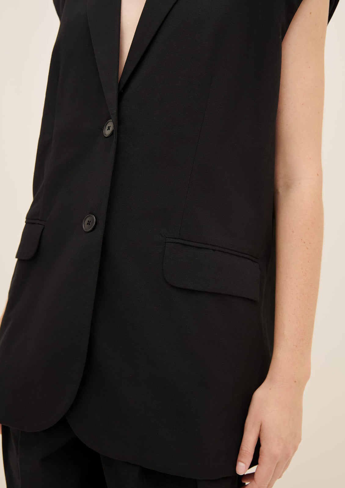 A woman wearing a black sleeveless blazer vest, without tie around waist.