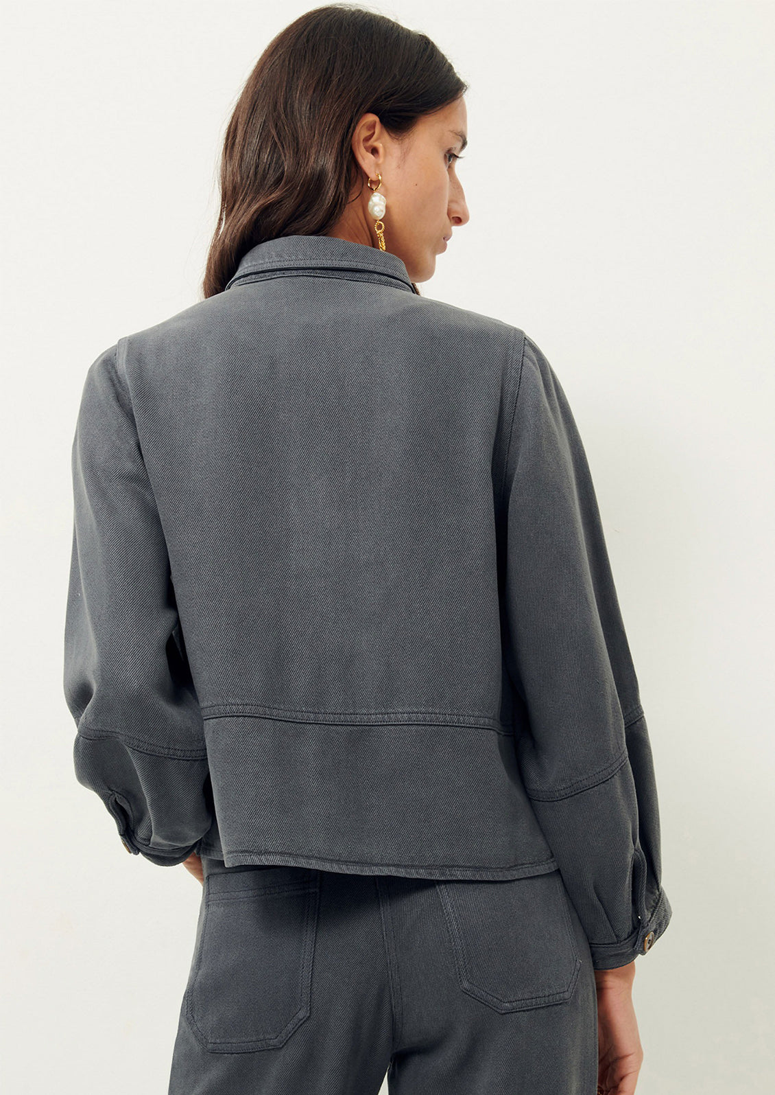 Woman wearing dark gray denim shirt jacket, seen from behind. 