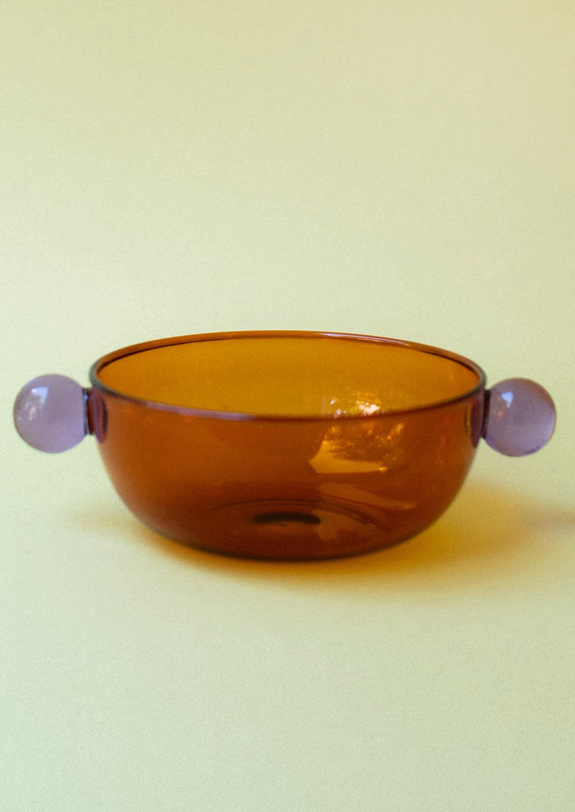 An amber glass bowl with lilac ball detail on sides.