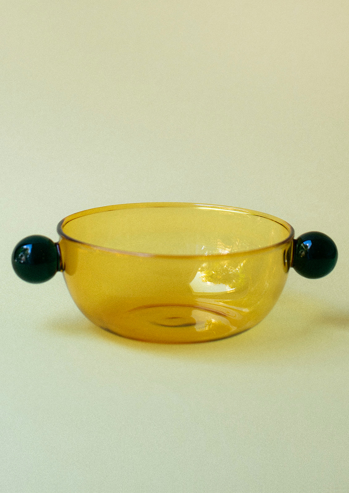 A yellow glass bowl with green ball detail on sides.