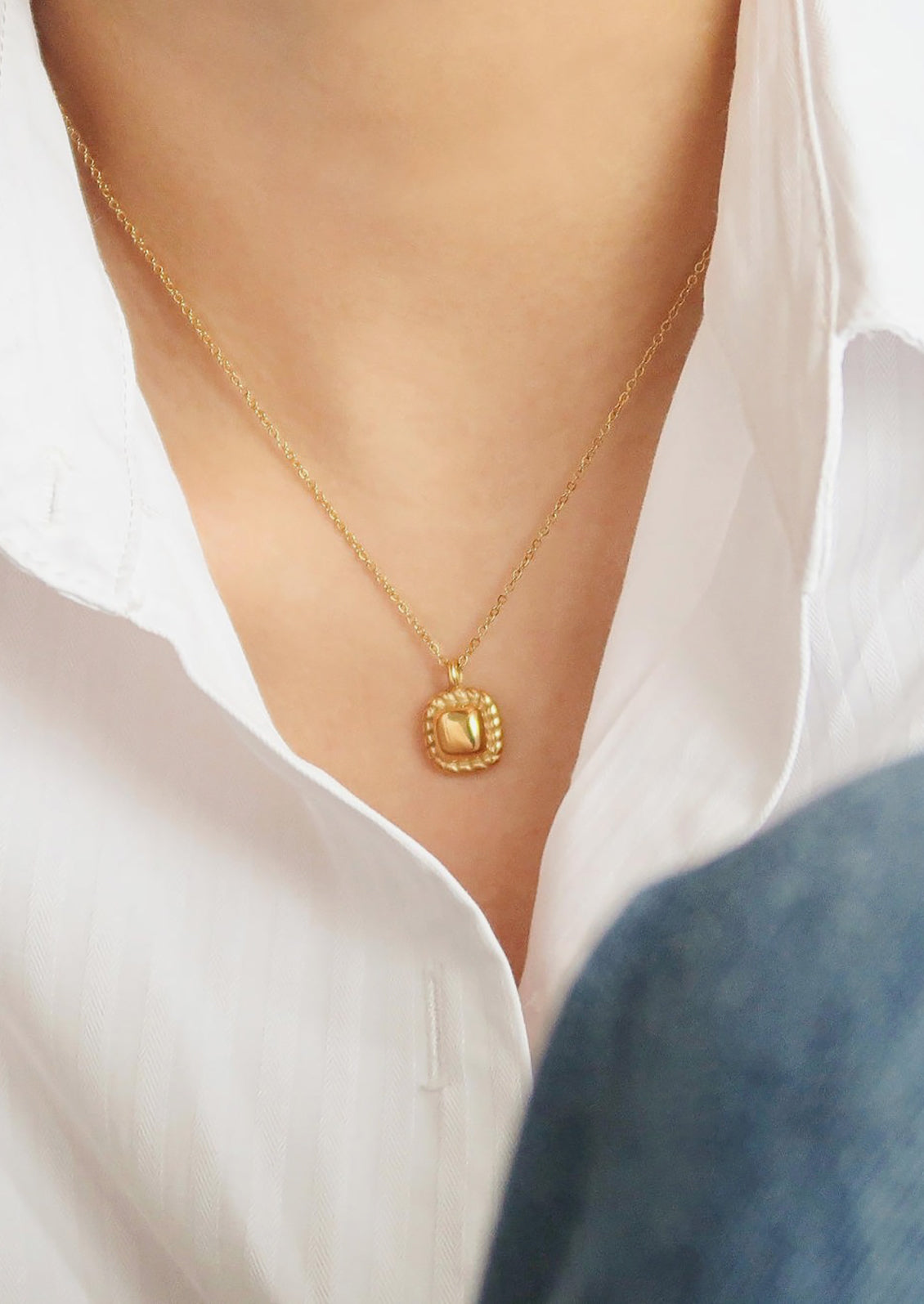A gold necklace with square vintage style charm.