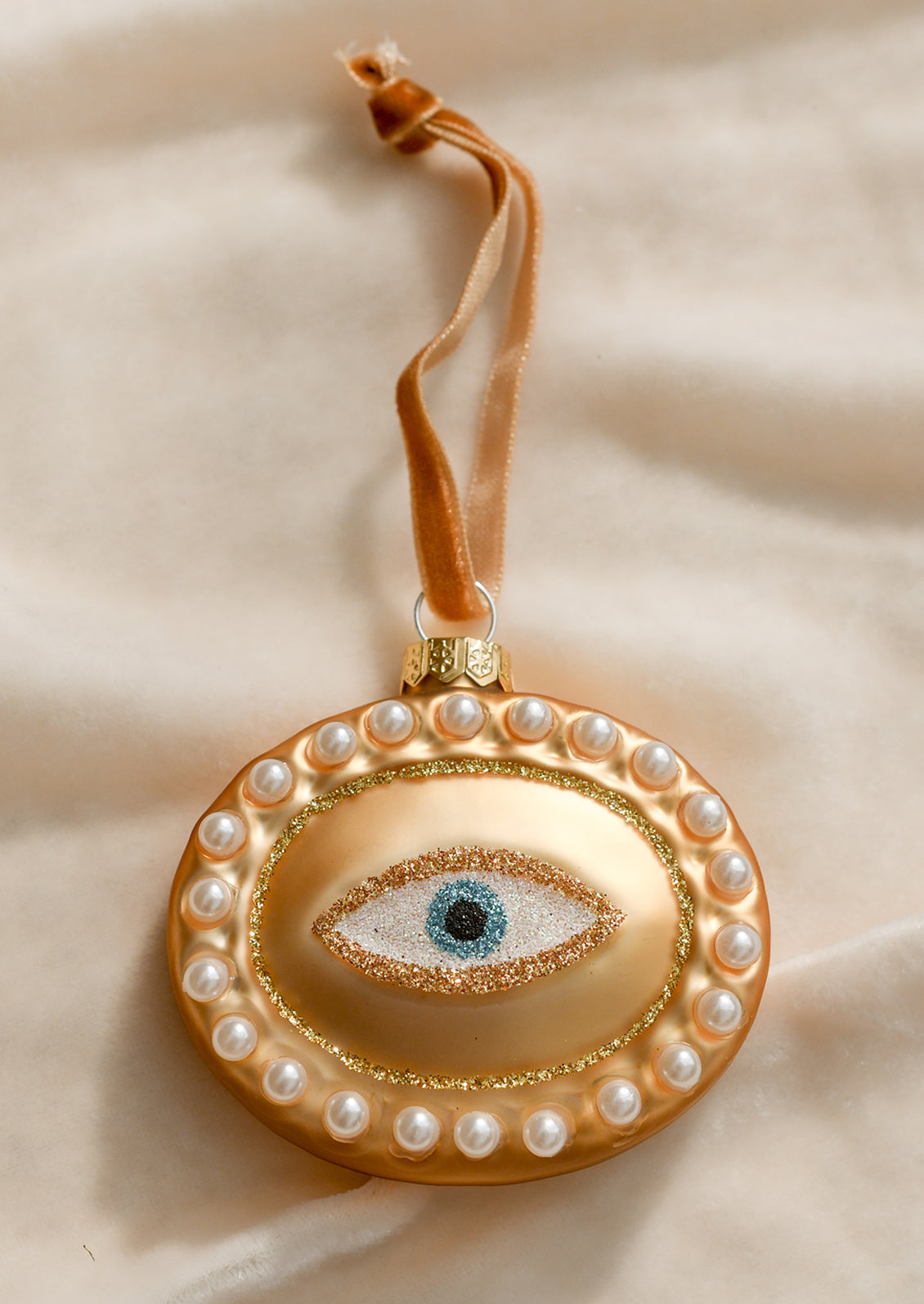 A glass ornament of gold oval with pearl border and glittery eyeball at center.