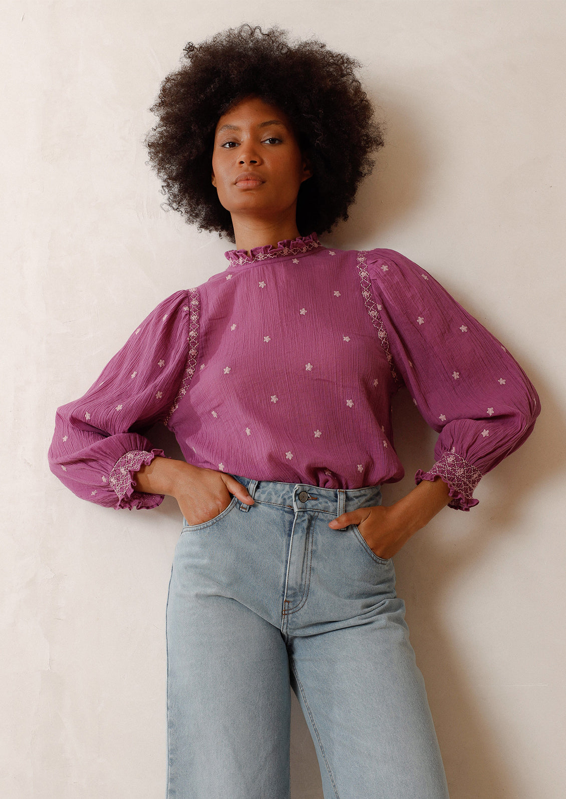 Woman wearing magenta top with embroidered details and blue jeans. 