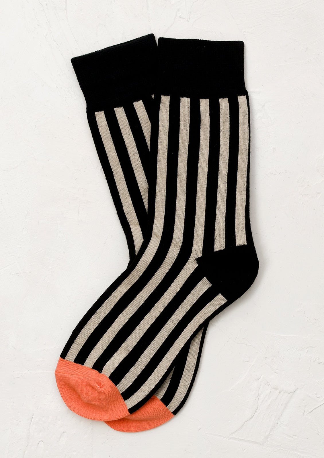 A pair of black socks with beige vertical stripes and orange cap toe.