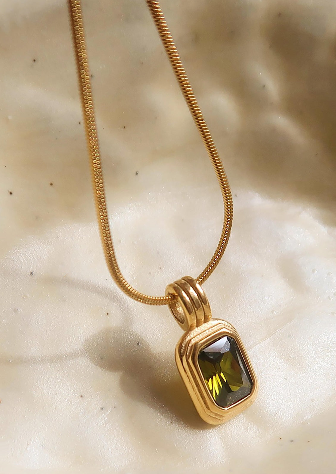 A necklace on round woven chain with rectangular pendant with olive green stone.