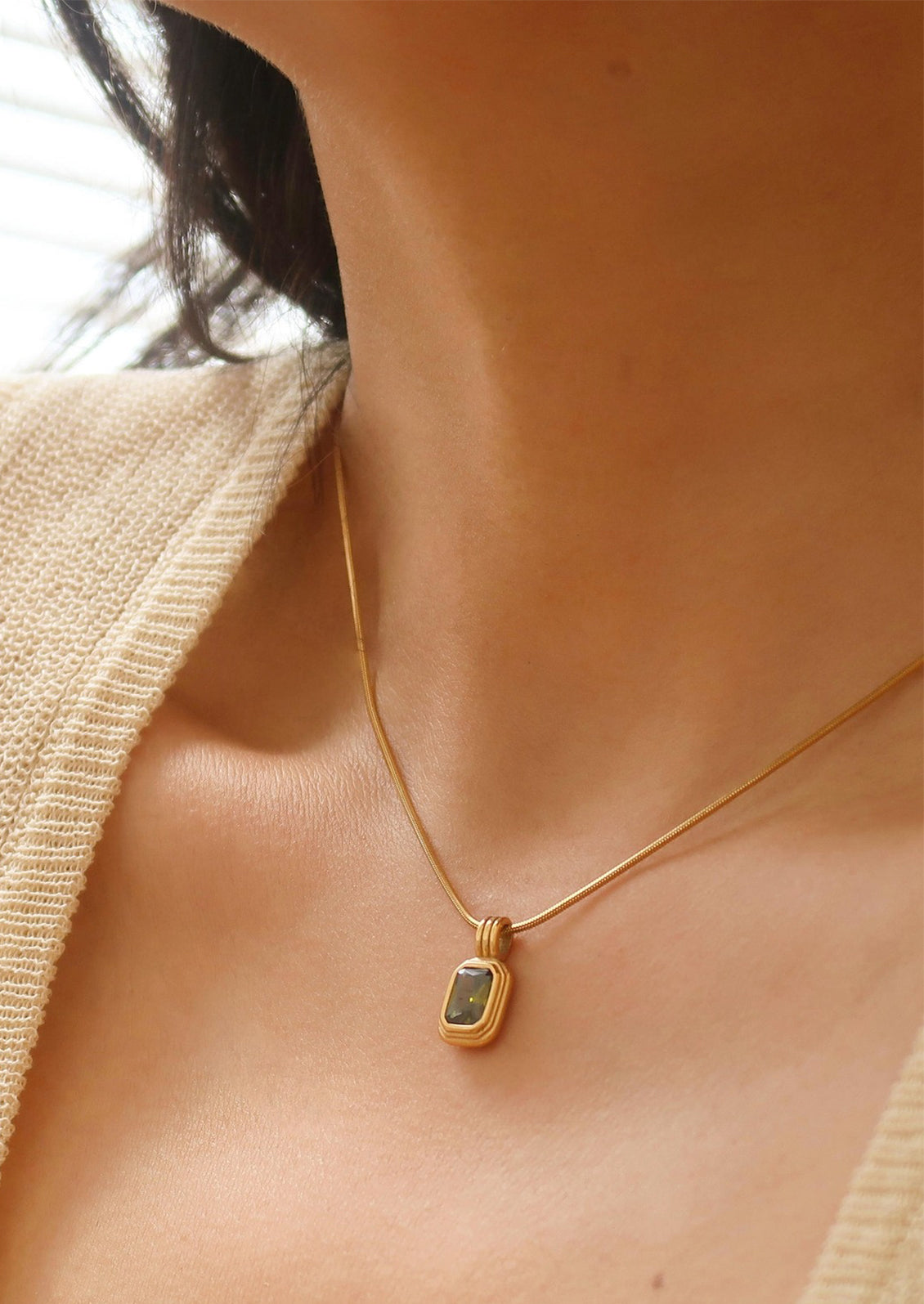 A necklace on round woven chain with rectangular pendant with olive green stone.