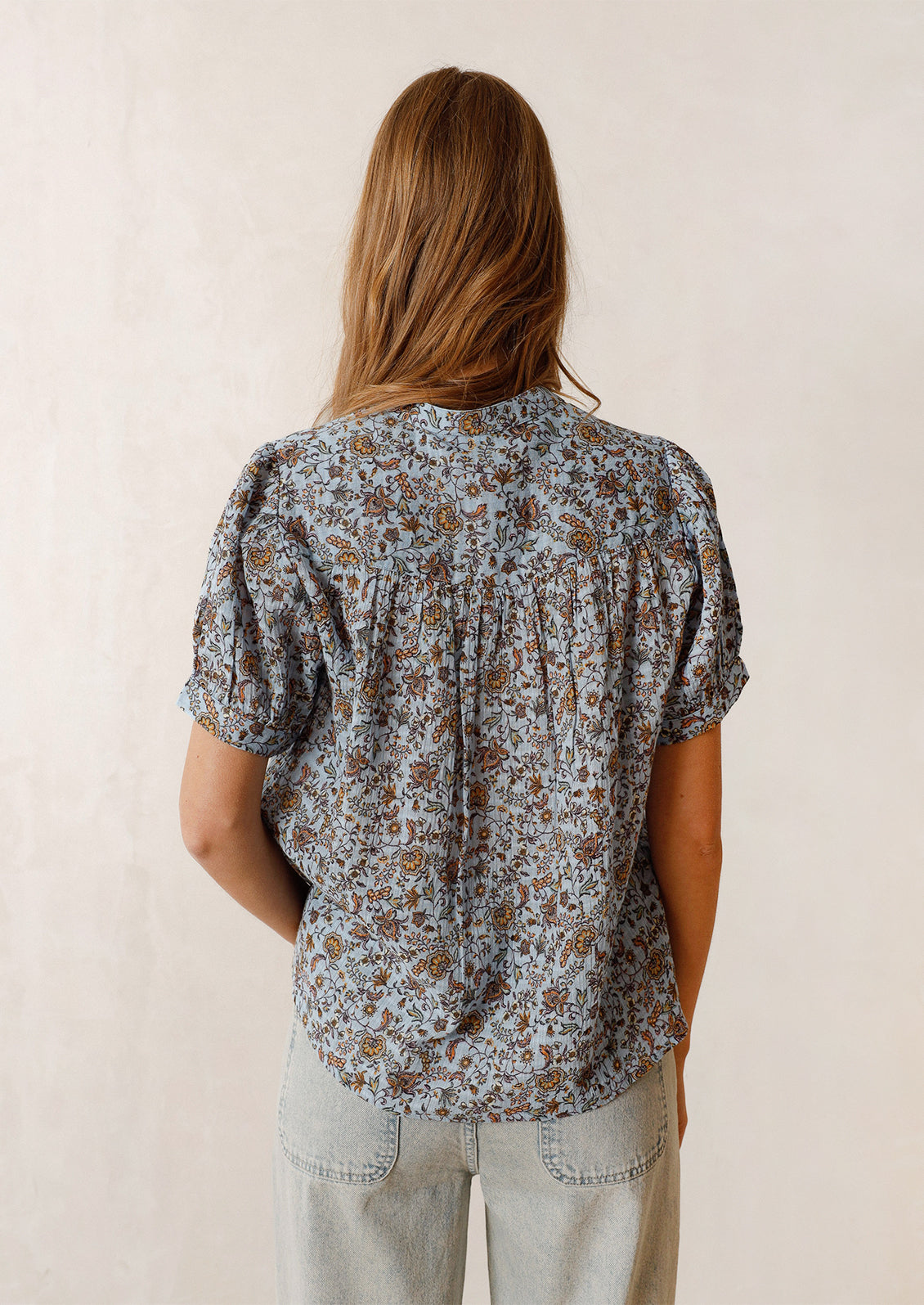 Woman wearing blue and brown printed top, seen from the back. 