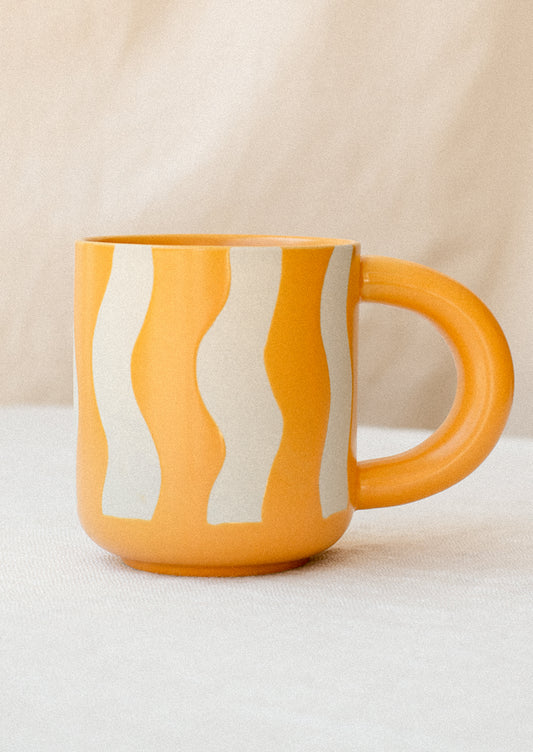 A ceramic mug in bright yellow with wax relief wavy stripe pattern.