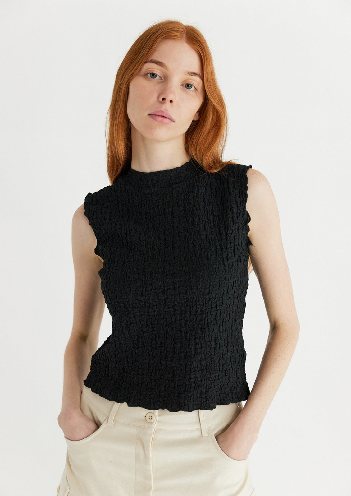 A woman wearing a sleeveless black top with crinkled texture.