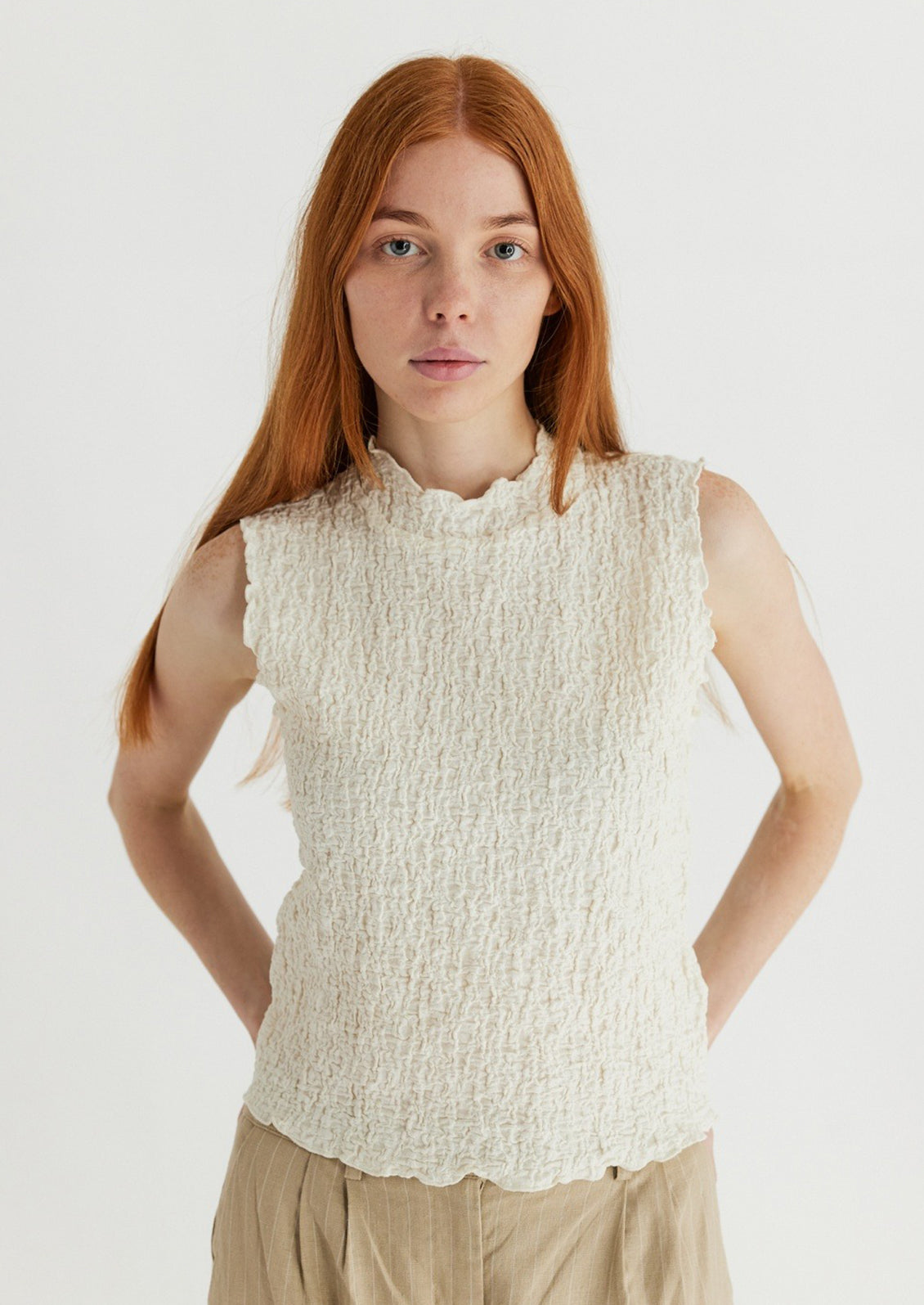 A woman wearing a sleeveless cream top with crinkled texture.
