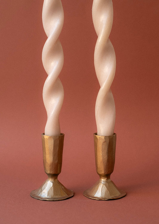 Two brass metal candlestick holders with a carved texture hold cream colored taper candles.