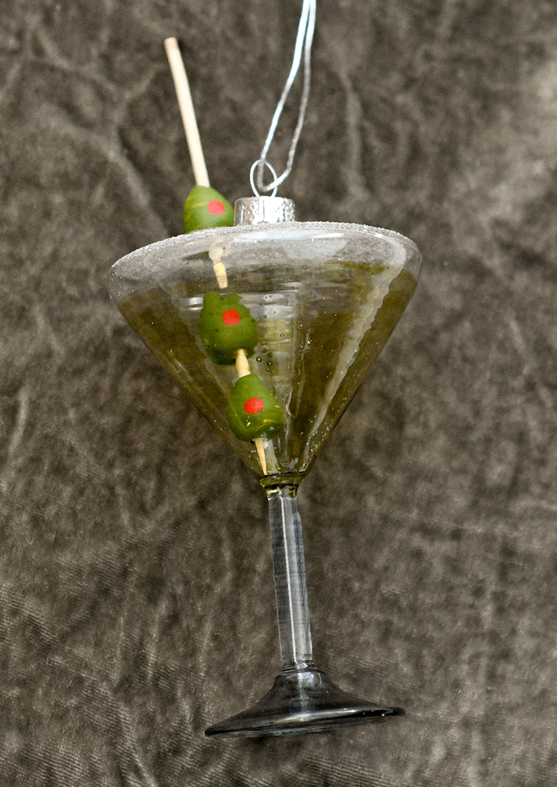 A glass ornament of a dirty martini with olives.