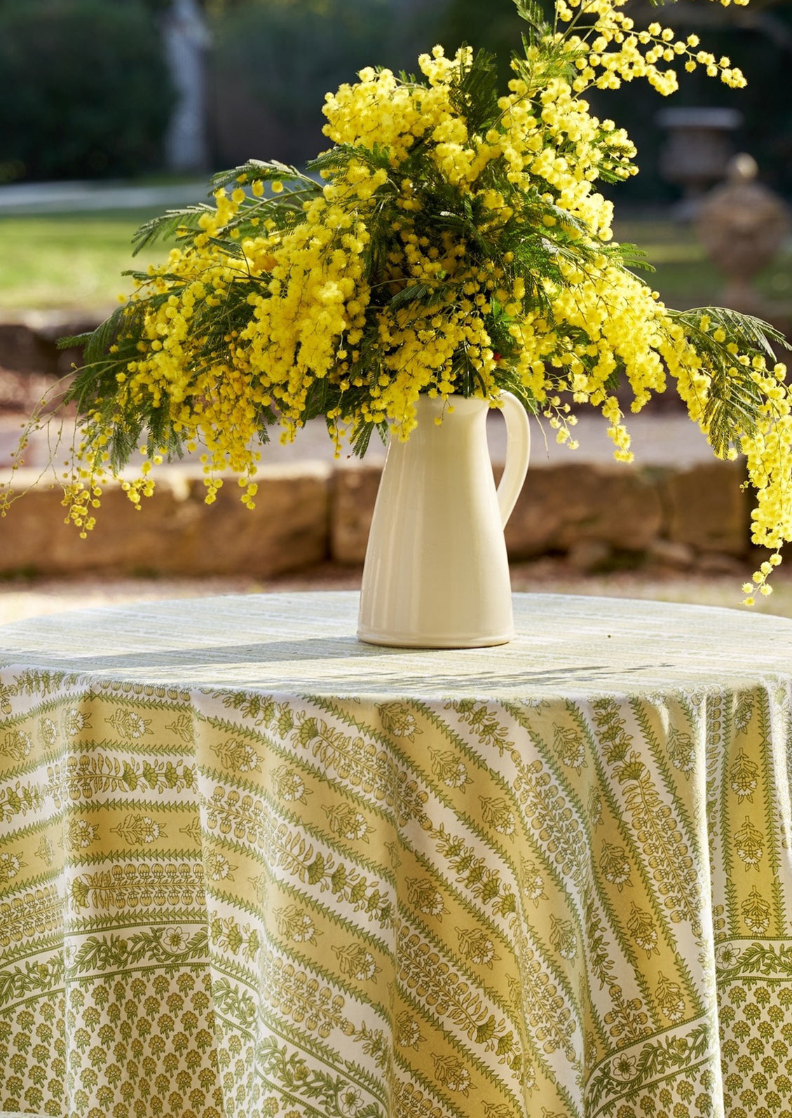 A block printed botanical patterned tablecloth in pastel yellow and green tones.