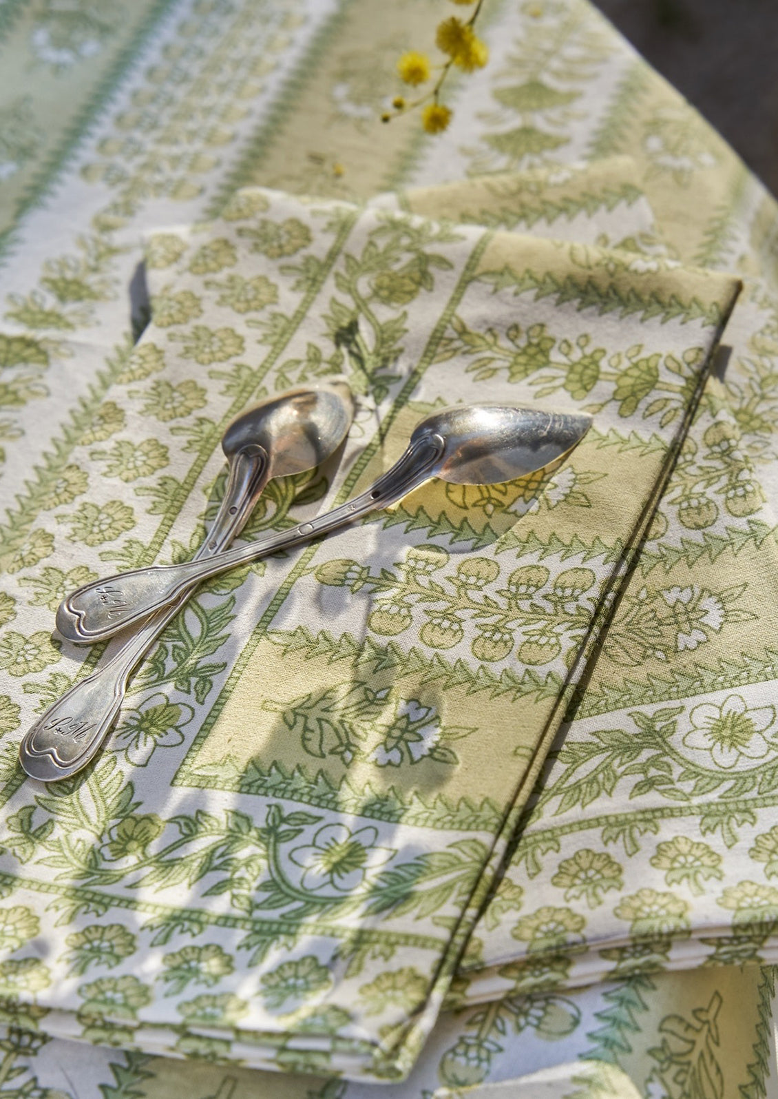 A block printed botanical patterned tablecloth in pastel yellow and green tones.