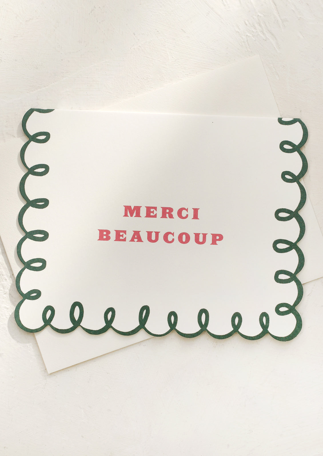 A scalloped edge card with pink lettering reading "Merci Beaucoup".