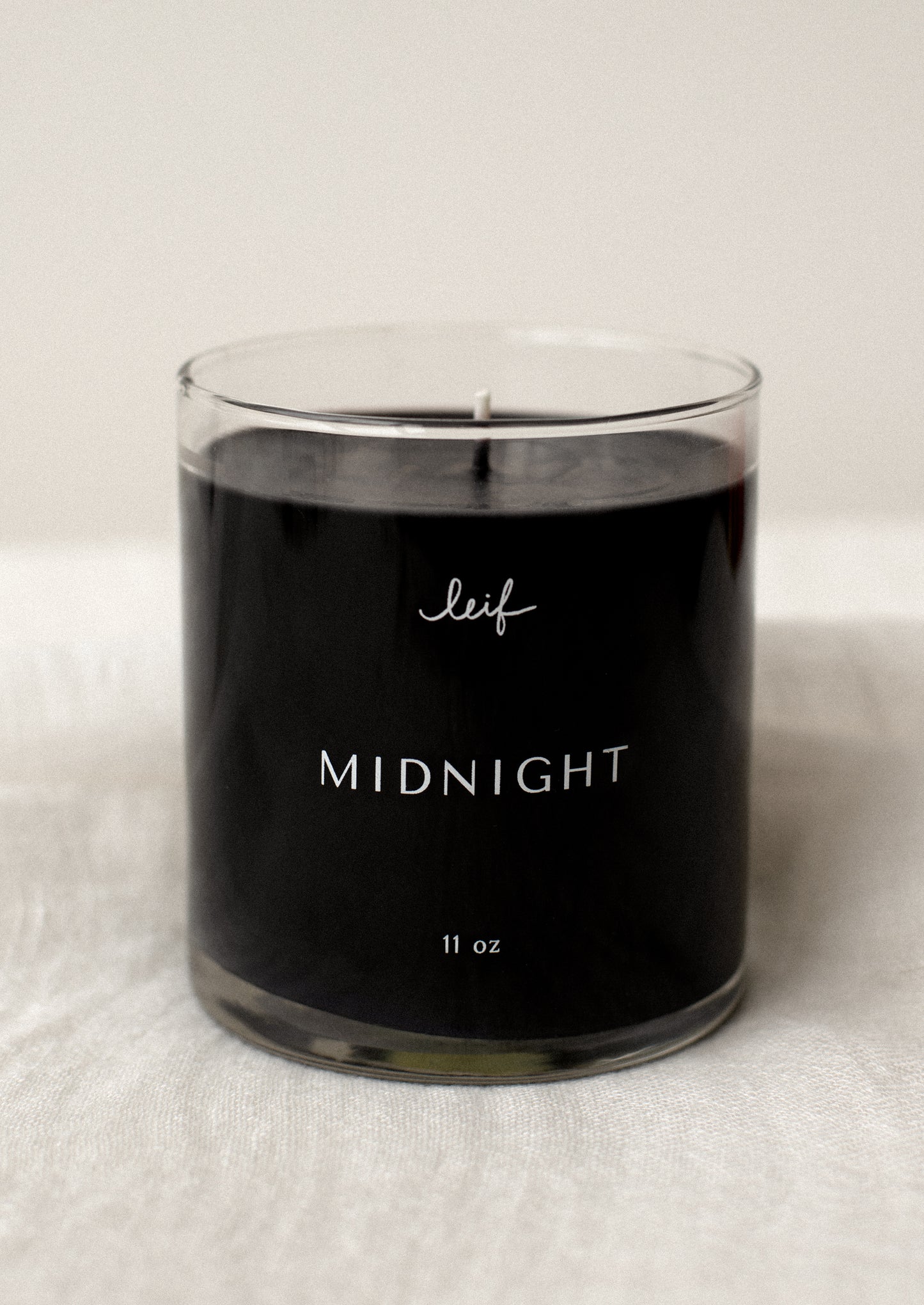 A black candle in clear glass jar labeled "Midnight".