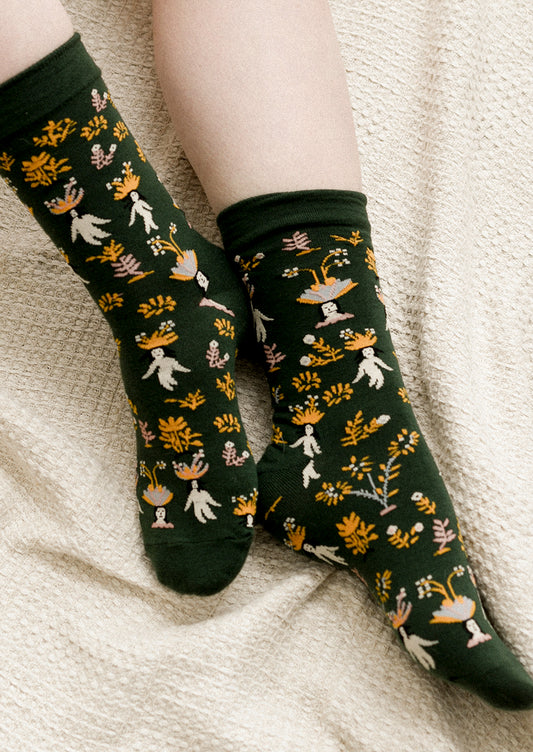 A pair of dark green socks with whimsical woman and flower print.